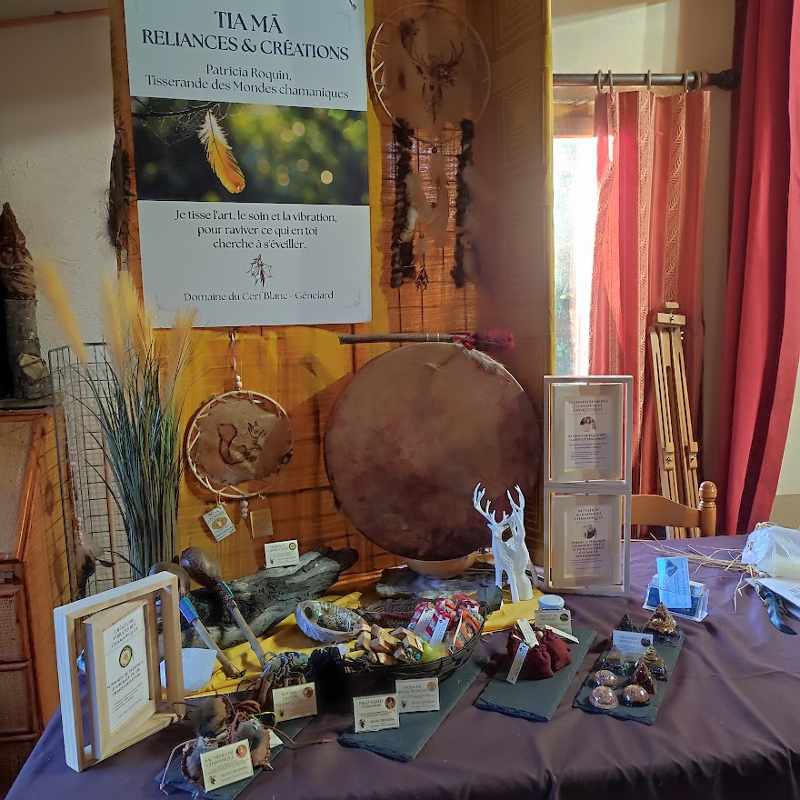 Tableau d’exposition artisanale avec attrape-rêves, tambour rond, décorations et brochures sur une table couverte.