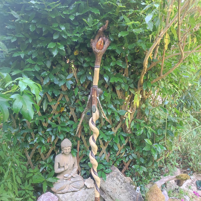 Branche spiralée, cristal, plumes, ruban, posée à côté d'une statue de Boudha dans un jardin de verdure