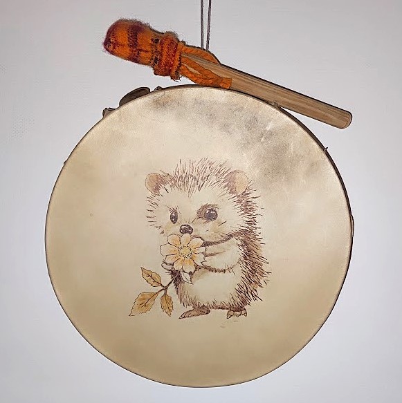 Tambour rond beige avec illustration d’un hérisson tenant une fleur, baguette en bois.