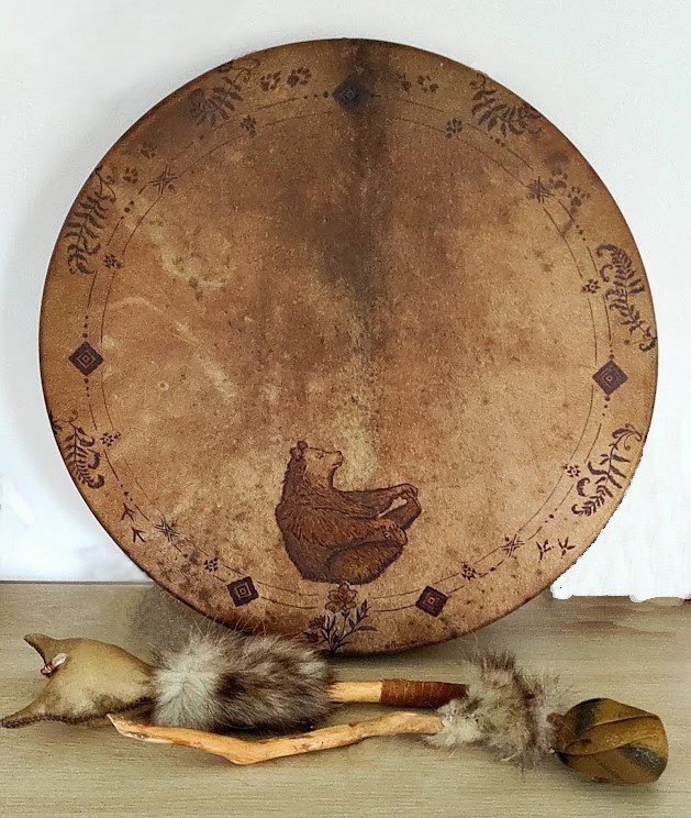 Tambour Cerf, peinture d'un ours, posée sur une table, avec un hochet et une mailloche.