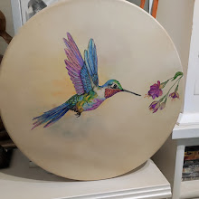 Tambour rond beige avec peinture d’un oiseau multicolore en vol et fleurs violettes, posé en vitrine.