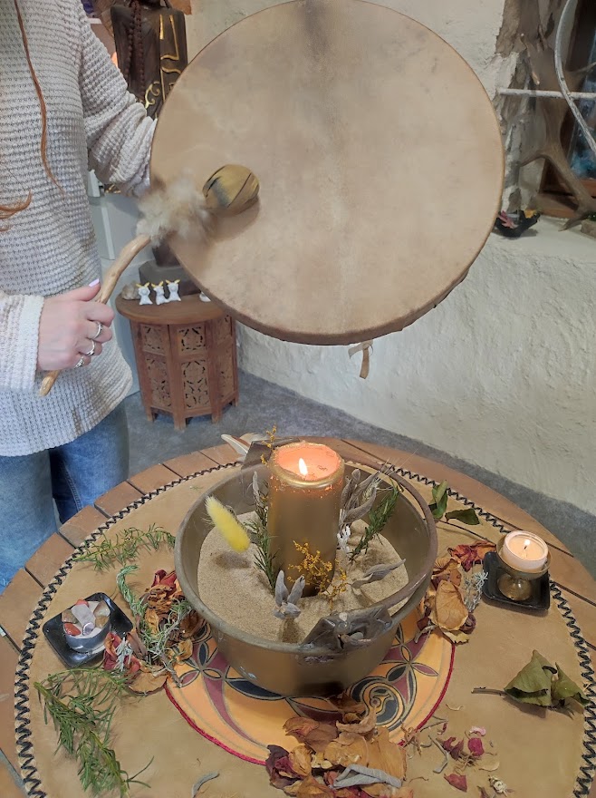 Bougie allumée, bol décoré de fleurs séchées, sur table ronde, et grand tambour.