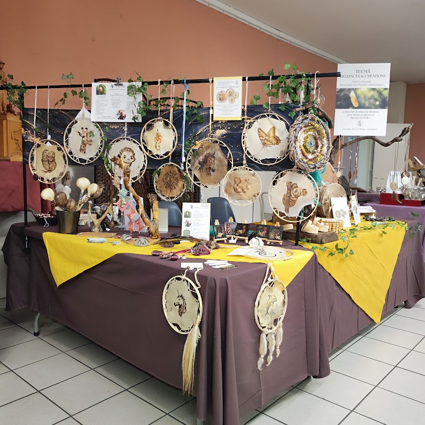 Stand artisanal avec attrape-rêves, cercles décorés, plumes et objets sur table couverte, en intérieur.
