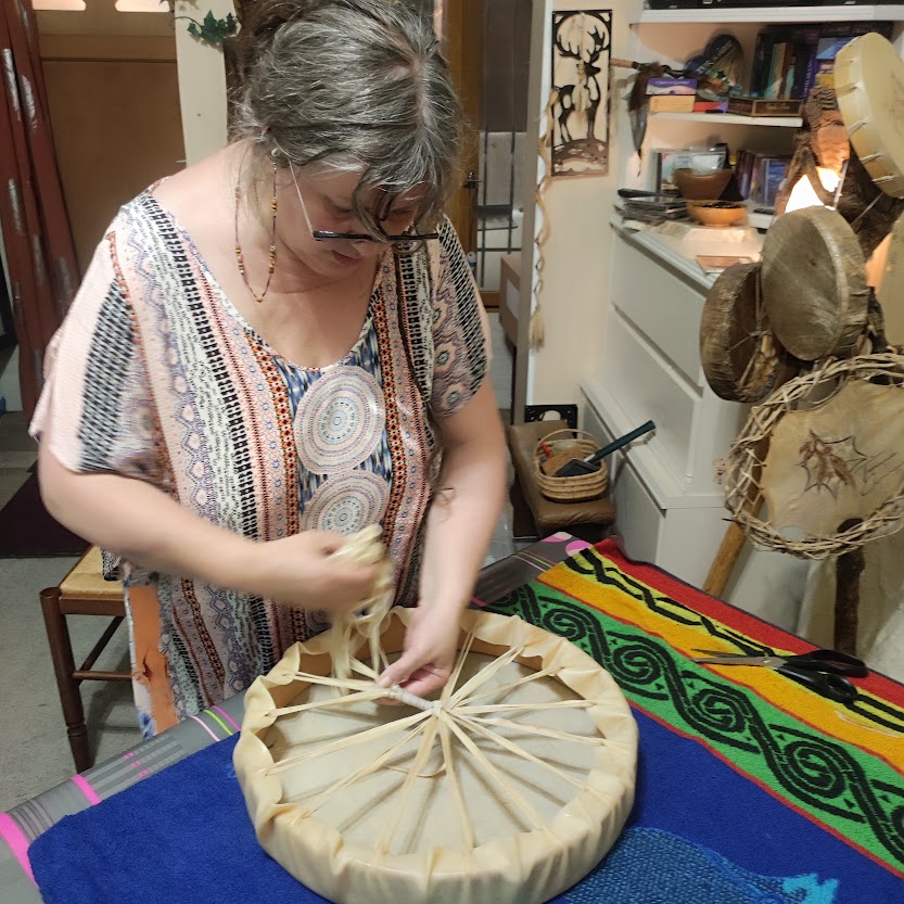 Femme tissant la lanière d'un tambour, dans un atelier rempli d’objets artisanaux.